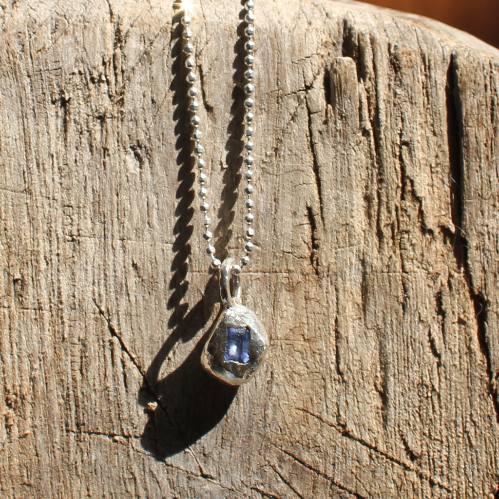 Silver necklace with a blue pendant on a wooden surface