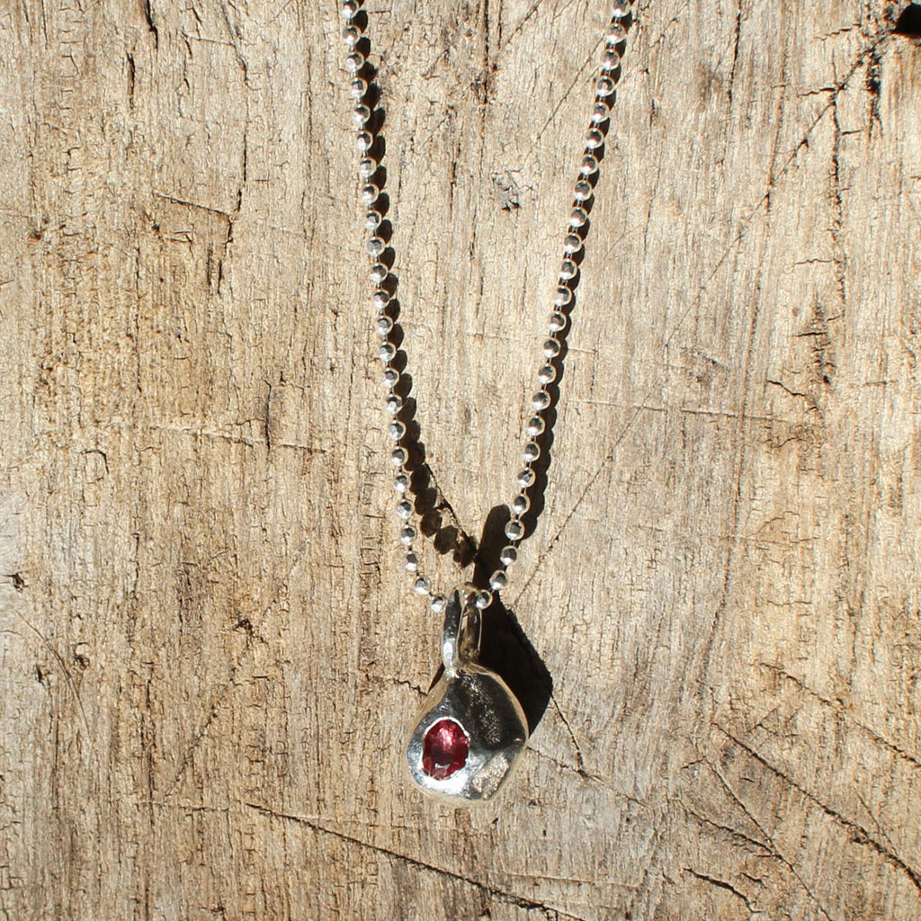 Silver necklace with a pendant featuring a red gemstone on a wooden surface