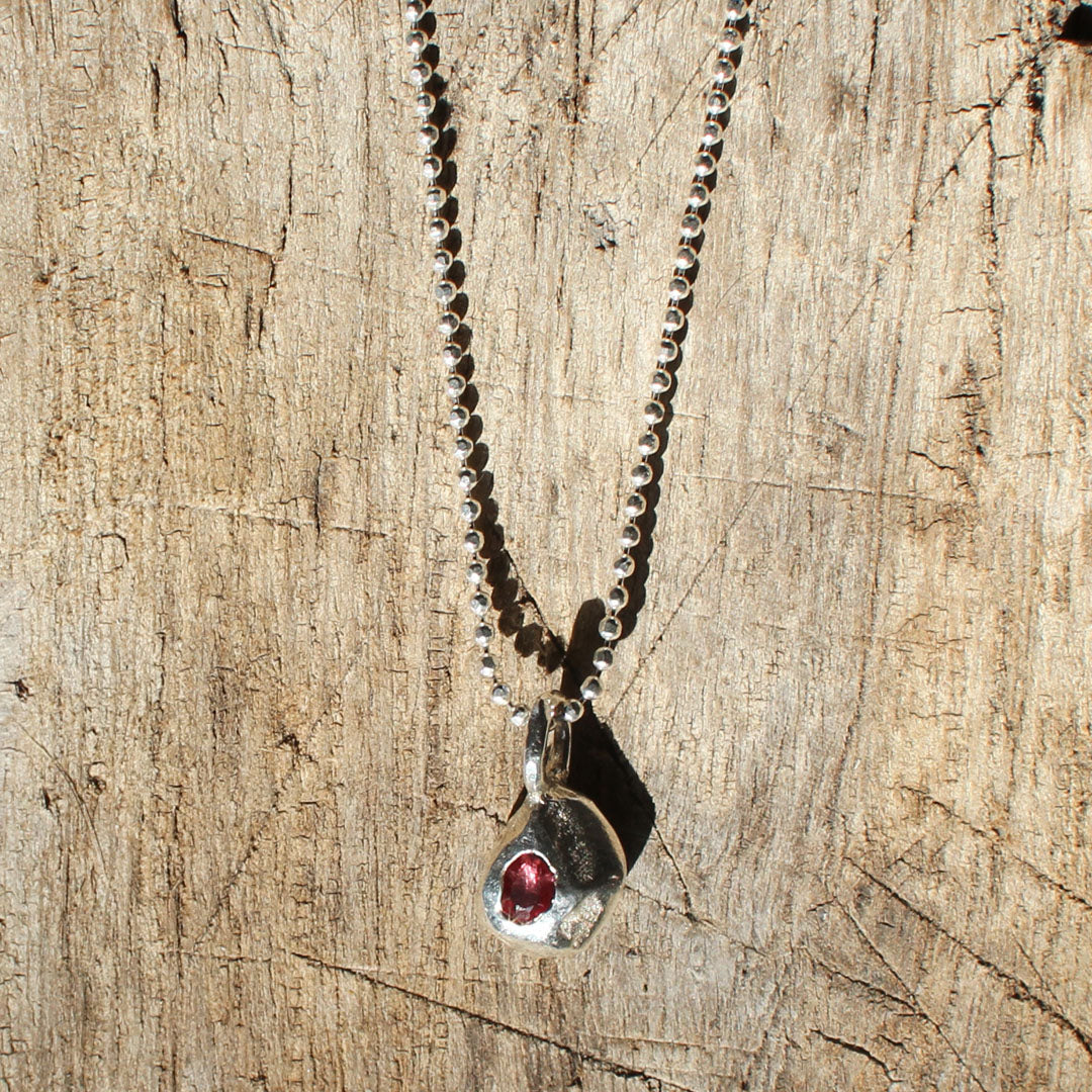 Silver necklace with a pendant featuring a red gemstone on a wooden surface